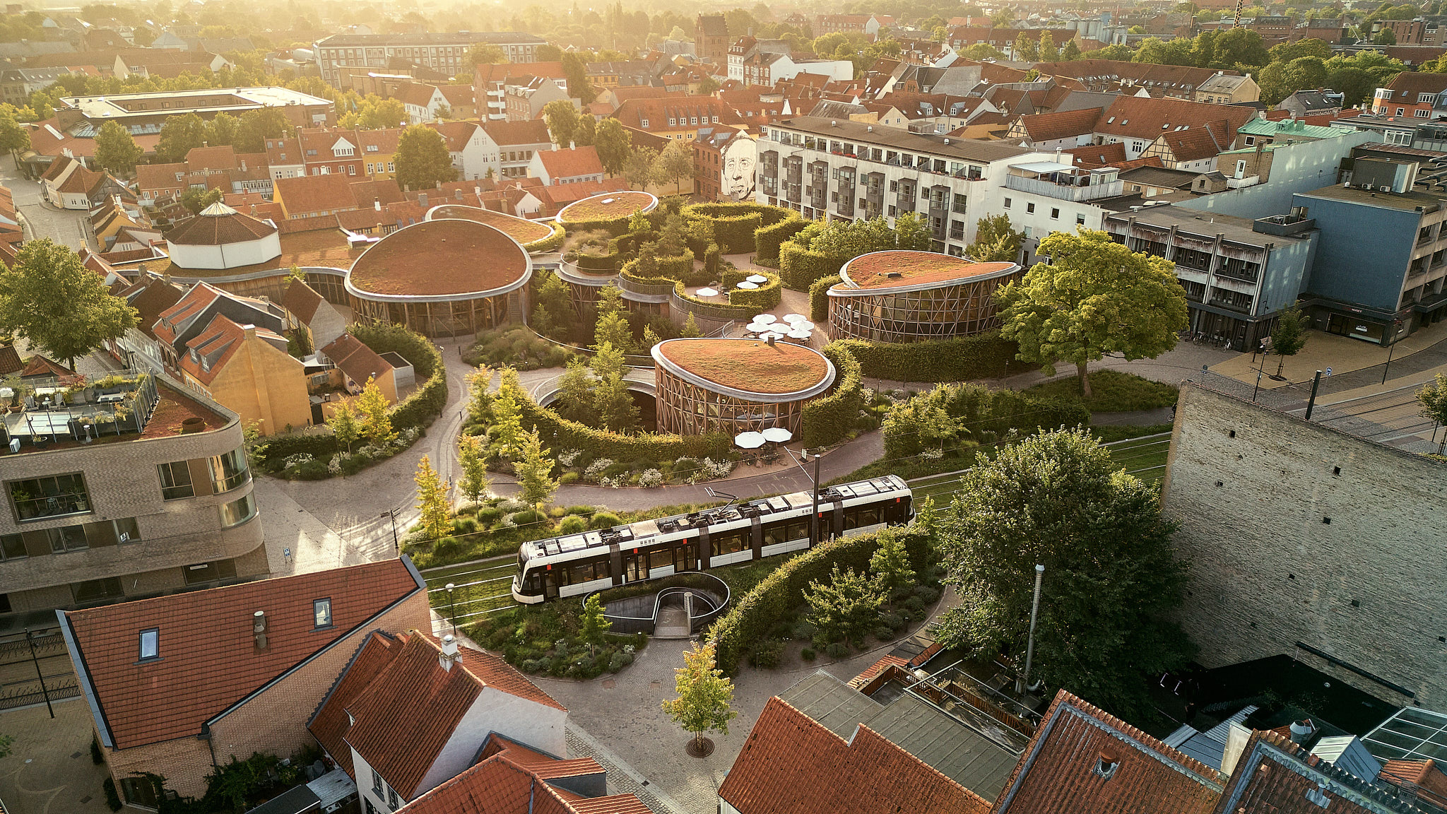 Moderne boligkompleks med grønne tage blandt historiske danske huse og sporvogn.
